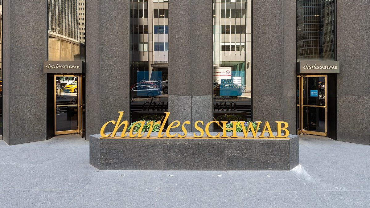The entrance of a Charles Schwab office, with the company name in gold letters on a stone planter between two glass doors